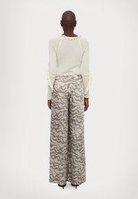 Pull en maille côtelée de couleur crème clair avec des accents volants ; associé à un pantalon beige à jambes larges avec un motif ondulé gris.