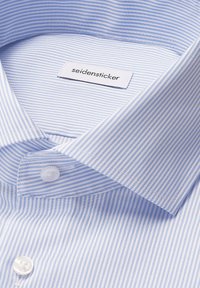Camicia a righe blu chiaro con colletto a camicia, bottoni bianchi e una texture intrecciata. L'etichetta riporta "seidensticker."