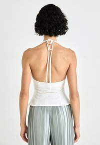 Top halter blanco con cintura ajustada, con un diseño atado en la espalda. Tela suave con una forma ajustada, complementado por pantalones plisados plateados.