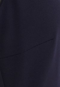 Mörk marinblått tyg med en texturerad, vävd yta. Har en liten, sydd ficka. Designen är enkel utan synliga mönster eller hårdvara.