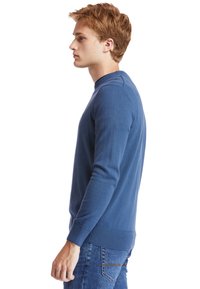 Maglione blu con scollatura rotonda, polsini e orlo a costine, design aderente, realizzato in un tessuto liscio. Indossato con jeans di denim.