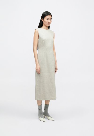 Ανοιχτό γκρι αμάνικο φόρεμα με ευθεία σιλουέτα, πλαϊνές τσέπες και μήκος μίντι, συνδυασμένο με γκρι κάλτσες και παπούτσια με κοφτή μύτη.