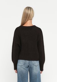 Brun strikket genser med bred utringning og senkede skuldre, kombinert med lyseblå høytlivsjeans. Teksturert fabrikkdetalj synlig.