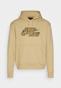 Sudadera con capucha beige con un bolsillo canguro frontal. Presenta un diseño de logo gráfico colorido en negro y amarillo con patrones de animales. Textura lisa.