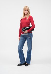 Top vermelho com decote ombro a ombro e mangas compridas, jeans azuis com corte evasê, mala preta de mão e sapatos planos pretos. Design simples, tecido leve e textura suave.