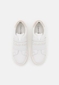 Sneakers bianchi con parte superiore in pelle liscia, strap elastico con marchio "Calvin Klein" e un accento in suede beige sul tallone.