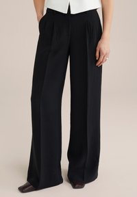 Pantaloni negri, cu picioare largi, cu pliseuri și un material texturat. Au buzunare laterale și o talie croită; asociați cu pantofi cu toc.