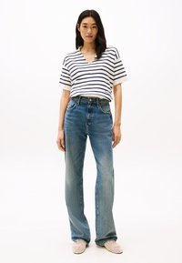 Ριγέ κοντομάνικο μπλουζάκι σε λευκό και ν αυτικό μπλε, συνδυασμένο με ανοιχτό μπλε ψηλόμεσα καμπάνα τζιν και καφέ πλεκτά παπούτσια slip-on.