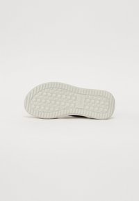 Black shoe sole with a textured, rubbery design. Features a grid pattern and branding detail near the heel. Smooth edges, light gray color.