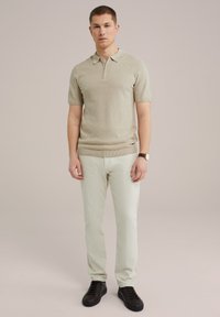 Knit polo shirt in light beige with a zip collar, paired with light green pants and dark sneakers. The fabric has a textured pattern.