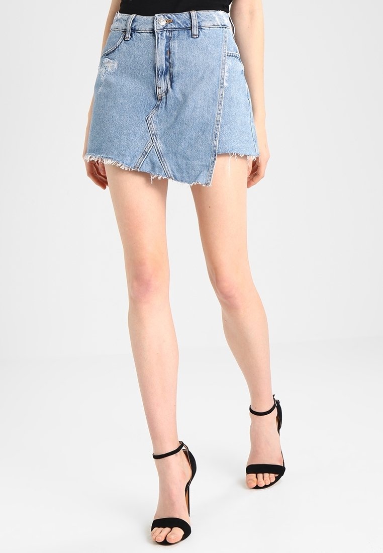 Minifalda de mezclilla azul claro con dobladillo deshilachado, que presenta una costura diagonal y diseño de cinco bolsillos, combinada con tacones negros de tiras.