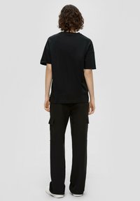 Schwarzes T-Shirt mit kurzen Ärmeln, kombiniert mit schwarzen Cargo-Hosen mit Seitentaschen. Der Stoff wirkt glatt und lässig.