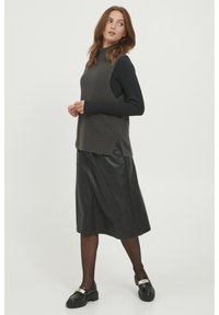 Szara rypsowa bluzka bez rękawów na czarną dopasowaną koszulę z długim rękawem, zestawiona z długą czarną skórzaną spódnicą i masywnymi czarnymi butami.