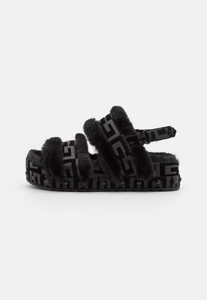 Sandale à plateforme noire avec doublure en fourrure, multiples brides avec un motif géométrique, et détails cloutés le long de la semelle.