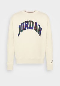 Sweat-shirt crème à manches longues, poignets côtes, et texte à carreaux coloré « JORDAN » en arc sur la poitrine.
