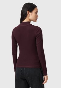 Burgunderfarbener Langarm-Top aus weichem, geripptem Stoff. Verfügt über eine figurbetonte Silhouette mit hohem Kragen und leicht schmal zulaufenden Ärmeln.