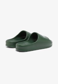 Zoccoli verdi in gomma con retro aperto, suole testurizzate e una finitura liscia. Presentano un logo bianco sul lato.