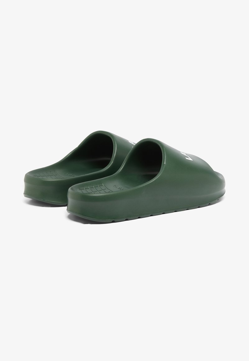 Grüne Gummischuhe mit offener Rückseite, strukturierten Sohlen und glatter Oberfläche. Mit einem weißen Logo an der Seite.