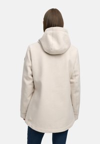 Vaalea huppari, joka on valmistettu pehmeästä kankaasta ja joka istuu rentosti. Hupparissa on kaareva helma ja pieni etiketti alareunassa.