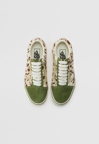 Baskets avec une tige en fourrure tachetée marron et crème, des accents en daim vert sur l'avant et sur les côtés, des lacets blancs et un logo sur la semelle intérieure.