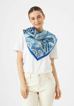 Seidenschal mit einem blauen Paisleymuster und Akzenten in Türkis und Gold, um den Hals drapiert über einem weißen Hemd.