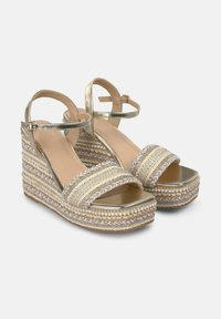 Hakken sandalen met metallic gouden banden en een geweven jute plateau. Heeft een brede voorkant band met decoratieve gevlochten en gedecoreerde accenten.