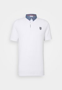 Polo blanc à manches courtes avec col en denim bleu, patte de boutonnage, et petit logo bouclier noir brodé sur la poitrine gauche.