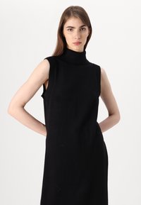 Μαύρο αμάνικο φόρεμα με ψηλό λαιμό, πλεκτό ύφασμα, εφαρμοστή σχεδίαση, ραβδώσεις στις λεπτομέρειες του κολάρου και των μανικιών, λεία υφή, ελάχιστες λεπτομέρειες.