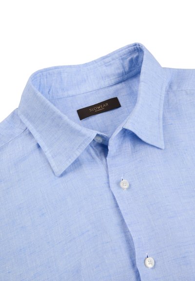 Camisa de lino azul claro con botones, cuello puntiagudo y dos botones blancos visibles cerca de la parte superior.