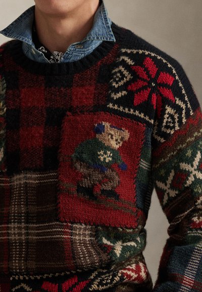 Stickad ulltröja med ett mönster av flerfärgad lapptäckdesign och ett björnmotiv. Färgerna inkluderar rött, grönt och marinblått, med olika mönster.