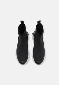 Czarne botki za kostkę wykonane z dzianiny z gładką, czarną czubkiem stopy i przezroczystą podeszwą. Posiadają pętelkę do łatwego zakładania.