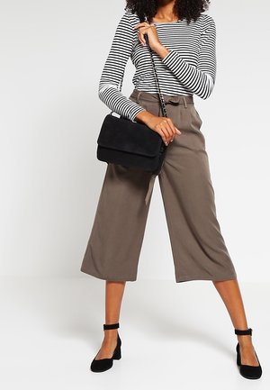 Bolso bandolera de ante negro con cierre de solapa, combinado con una camisa de manga larga a rayas blancas y negras y pantalones anchos marrones.