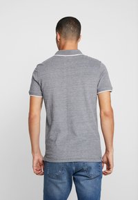 Grå polo skjorte med hvite detaljer på kragen og ermene, laget av teksturert stoff, sammen med blå denim jeans.