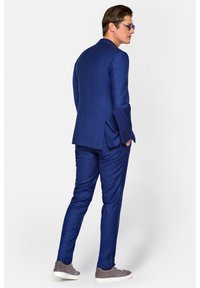 Niebieska marynarka w kratę zestawiona z pasującymi spodniami. Wyróżnia się gładką teksturą, dopasowanym krojem i szarymi trampkami.