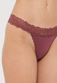String en dentelle bordeaux avec un tissu lisse et extensible et des détails raffinés le long de la taille, présentant un design en V classique.