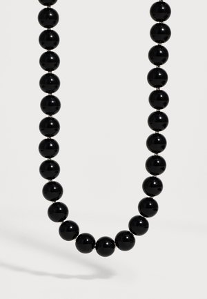 Collar de una sola cadena con grandes cuentas negras redondas y brillantes, espaciadas uniformemente sobre un fondo claro y neutro.