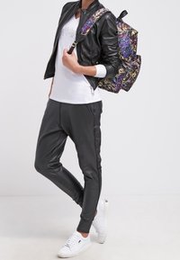 Černá kožená bomber bunda, bílá grafická trička, šedé tepláky, bílé tenisky a batoh s mnoha vzory. Neformální městský styl.