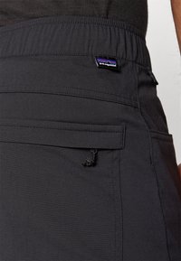Sorte shorts med elastisk liv, med en liten lomme og snordetalj. Laget av lett stoff med synlig slitesterk søm.