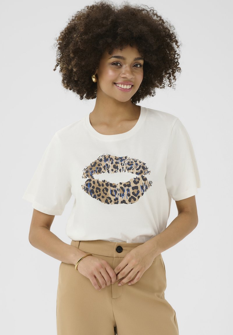 T-shirt blanc à manches courtes avec un graphisme de lèvres en imprimé léopard dans des tons beige, noir et bleu. Material en coton doux, coupe décontractée.