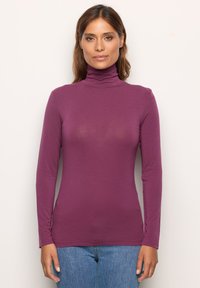 Langärmliges Rollkragenoberteil in einheitlichem Dunkelpurpur, aus weichem Material gefertigt. Besitzt ein enganliegendes Design und eine glatte Textur, kombiniert mit hellblauen Jeans.