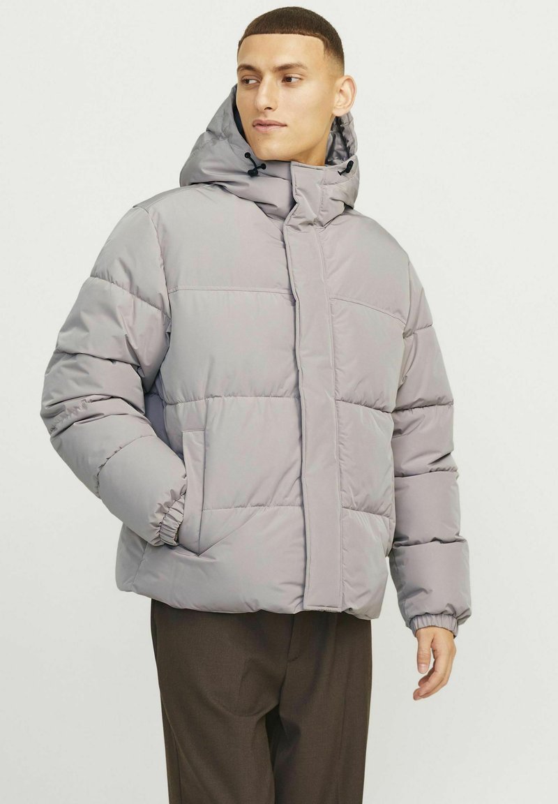 Puffet grå jakke med hætte, med elastiske manchetter og lynlås foran. Materialet ser blødt og isoleret ud. Enkel quiltet design.