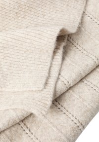 Blødt beige strikket stof med ribbet manchet ved siden af et tekstureret diamantmønster i samme lyse beige uldmateriale.