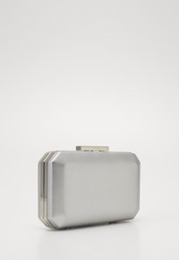Clutch argento metallico con design angolare, texture liscia e chiusura a scatto. Presenta una superficie riflettente subtile e dettagli in hardware color oro.