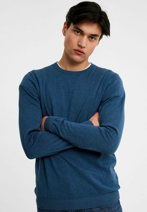 Pull en maille bleu avec un col rond, des manches longues et des poignets et un ourlet côtelés. Le tissu semble doux et a une texture fine.