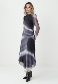 Długa szara sukienka z gradientowym wzorem, z marszczeniami i przezroczystymi długimi rękawami, w połączeniu z czarnymi butami na obcasie w kształcie czubków.