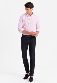 Heren overhemd met knopen, roze met witte strepen, gecombineerd met een donkere spijkerbroek. De outfit heeft een slim fit en zwarte schoenen.