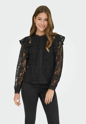 Black lace top featuring ruffled sleeves, a scalloped neckline, and decorative front detailing. Paired with black fitted pants.