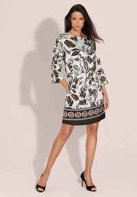 Blumenmusterkleid mit langen Glockenärmeln, einem hellblauen Grundton und einem schwarzen Saum mit kreisförmigen Akzenten. Hergestellt aus glattem Stoff.