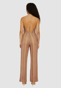 Tuta a righe nei toni bronzo e pesca, con scollatura all'americana, schiena scoperta e gambe ampie con una finitura testurizzata.