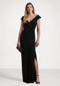 Svart, off-shoulder kvällsklänning med tvinnad midjedetalj, hög slits till låret och en glittrande yta. Clutch-väska med guldhardware ingår.